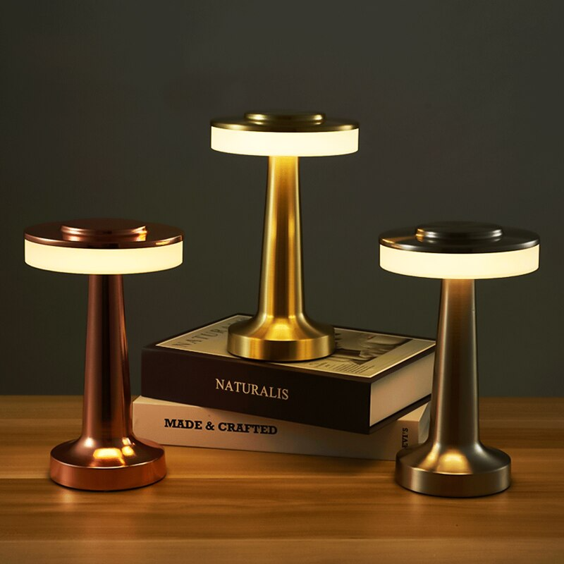 Three wireless rechargeable table lamps in gold, silver, and rose gold displayed together on a wooden surface