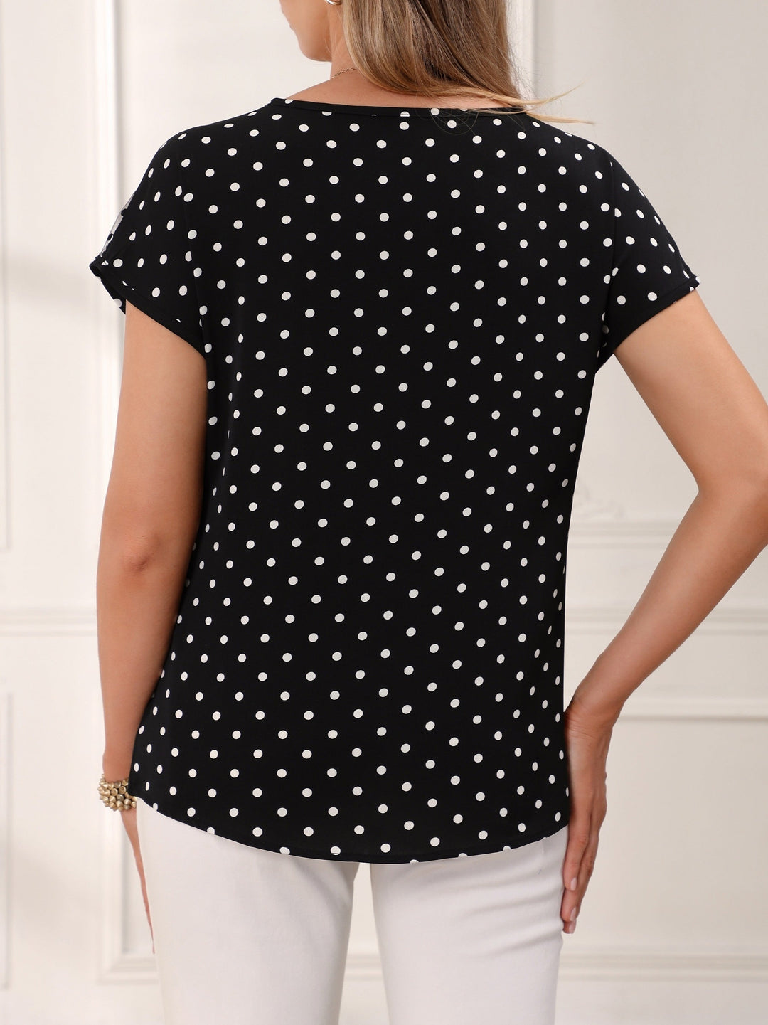 Back view of a woman wearing a black short-sleeve polka dot blouse.
