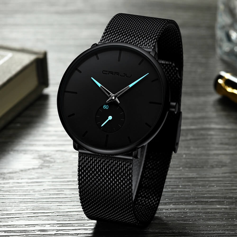 Men's minimalist luxury quartz watch in black with blue hands on dark wooden table