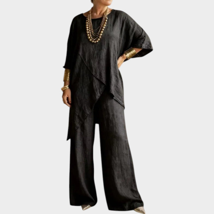 Woman wearing black asymmetrical two-piece matching set with layered gold necklaces