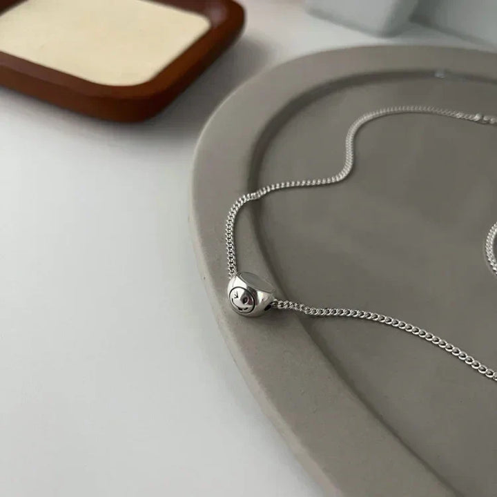 Close-up of the silver chain and smiley pendant resting on a tray