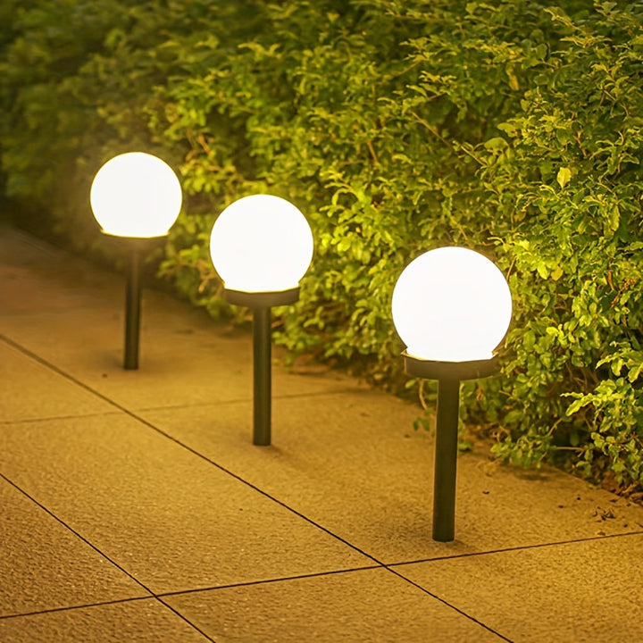 Three spherical solar LED garden lights glowing along a pathway next to green foliage at night
