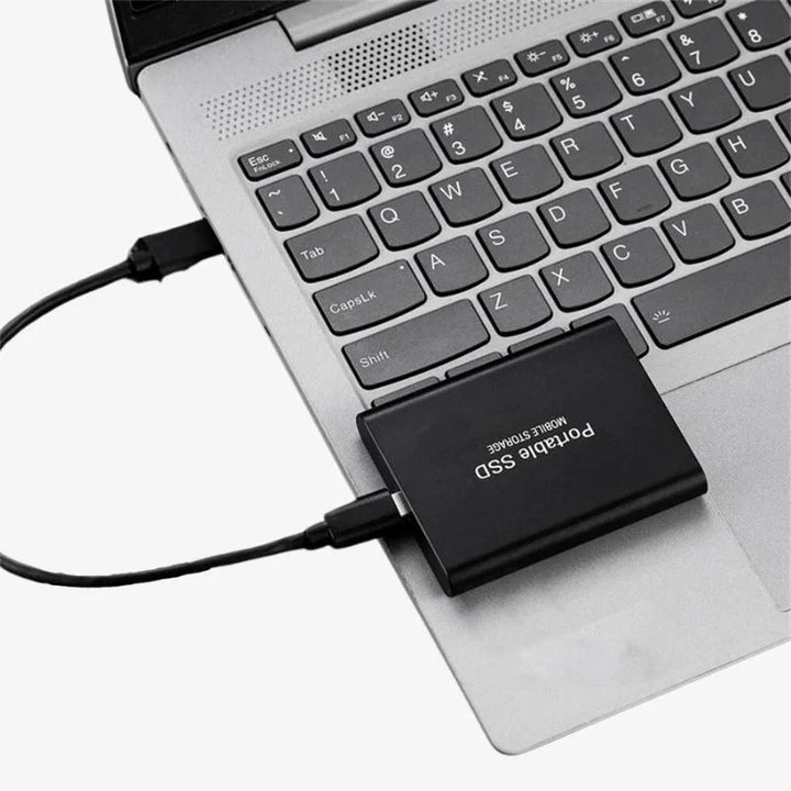 Black portable SSD connected to a silver laptop workspace