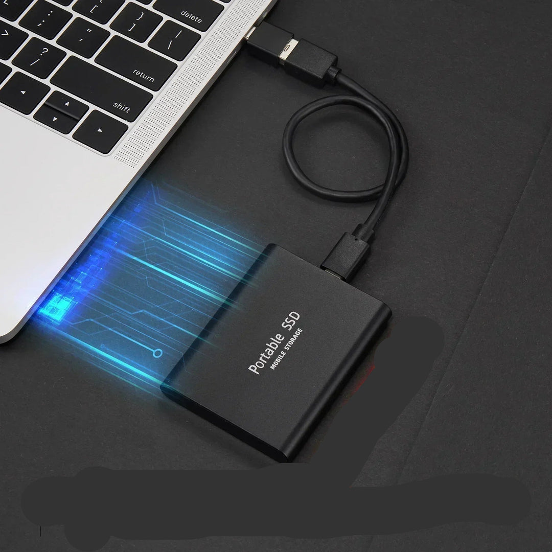 A black portable external solid state drive connected via USB cable to a laptop keyboard.