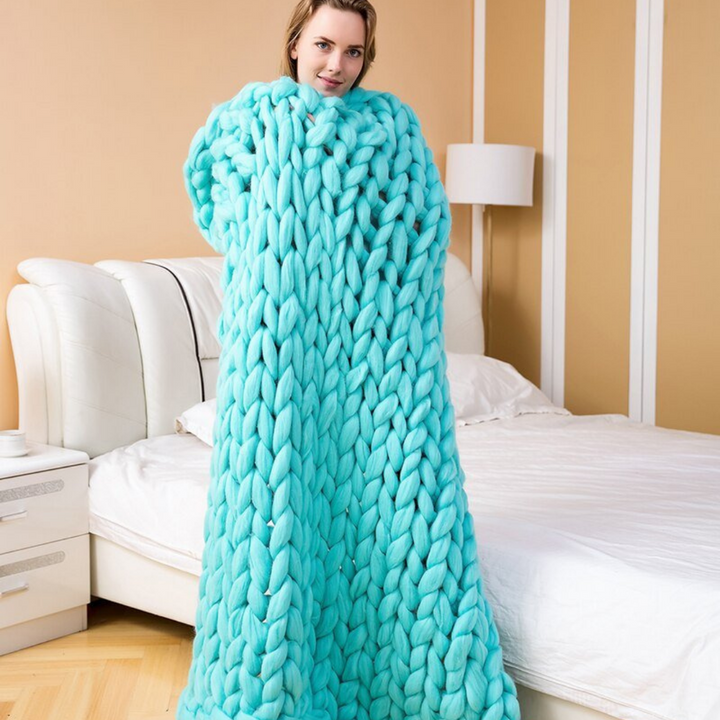 Woman standing in a bedroom wrapped in a bright aqua chunky knit blanket