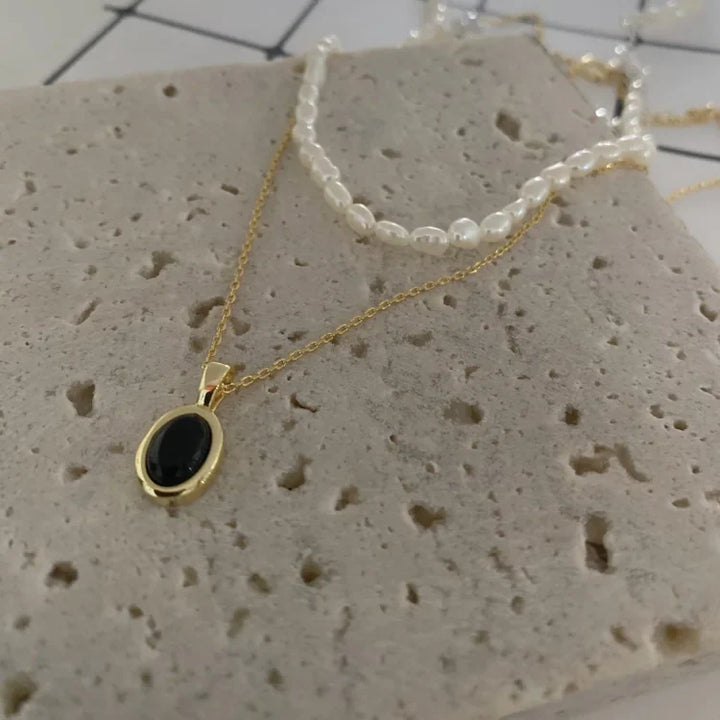Close-up of layered pearl and dark stone pendant necklace set on stone surface