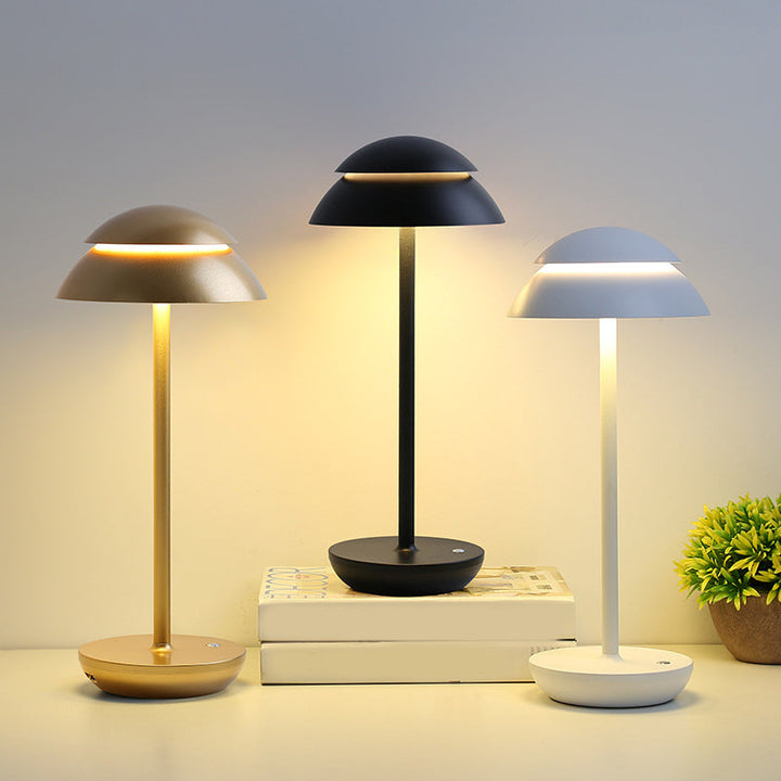 Three cordless LED table lamps in gold, black, and white displayed on top of books.