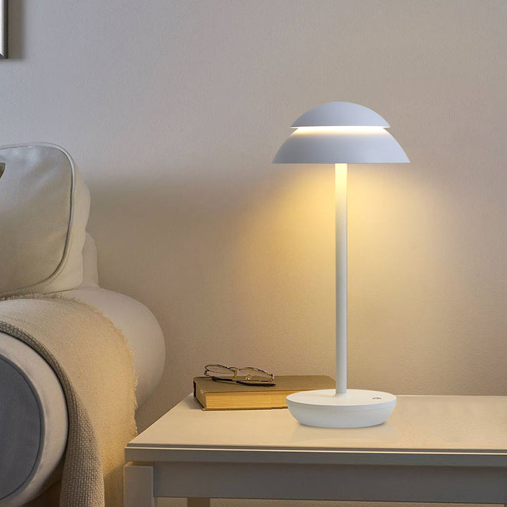 White cordless LED table lamp illuminating a modern bedside table next to a book.
