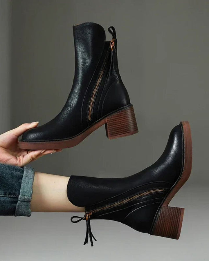 Hand holding a black block heel boot highlighting the sturdy wooden heel and sole