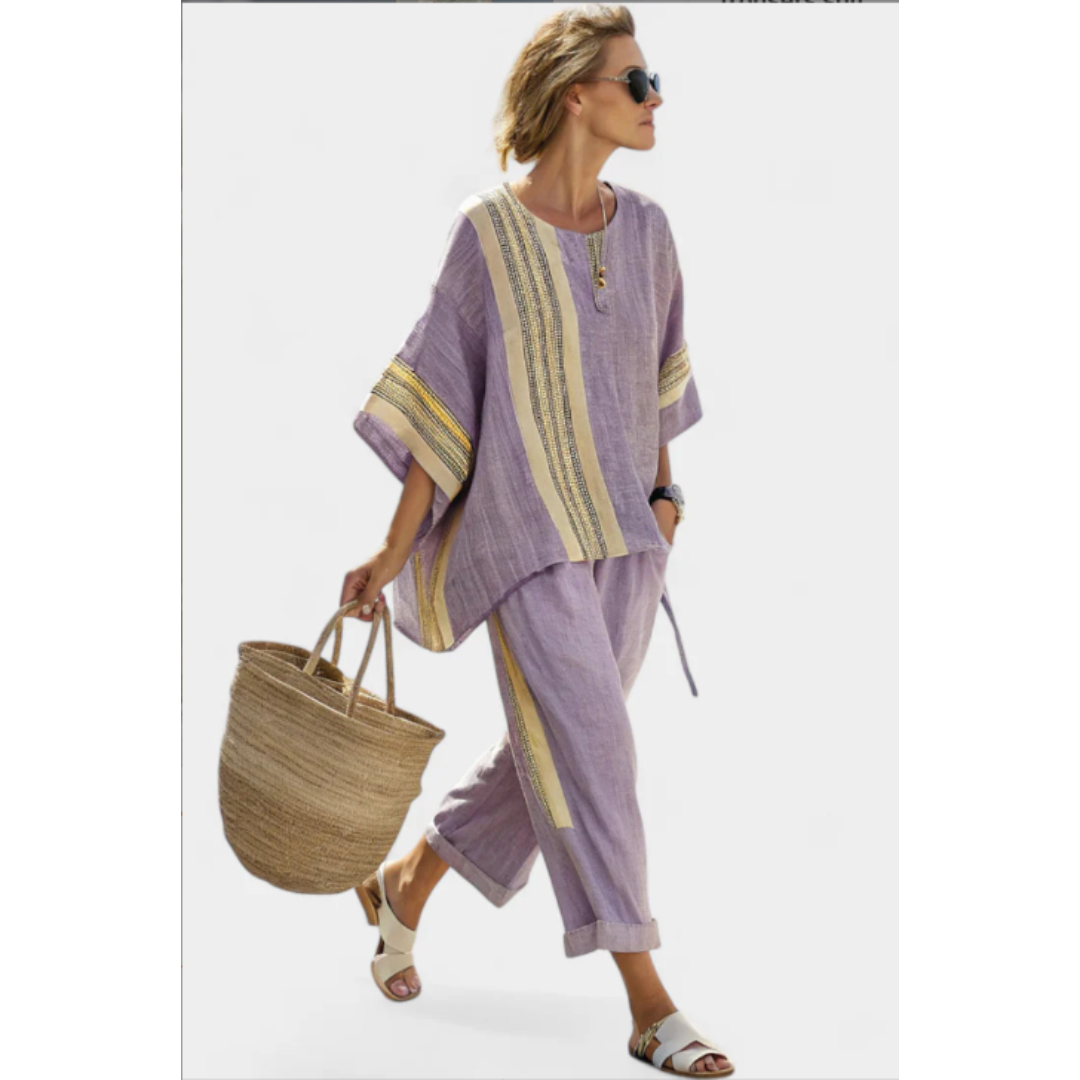 Model wearing a purple striped two-piece outfit with trousers and a top holding a woven bag.