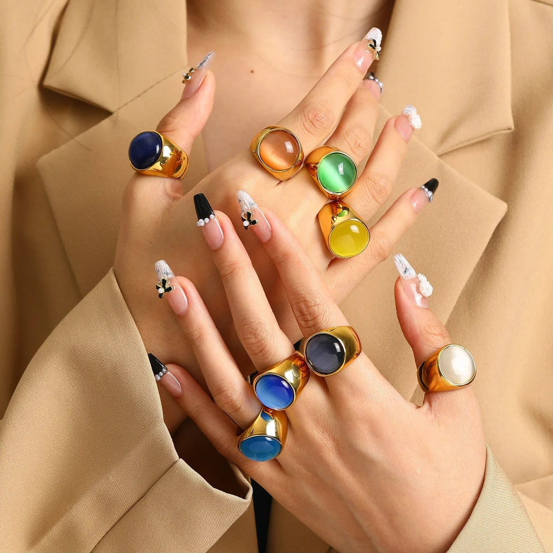 Close-up of a hand wearing multiple colorful cat's eye gemstone statement rings in various vibrant shades.