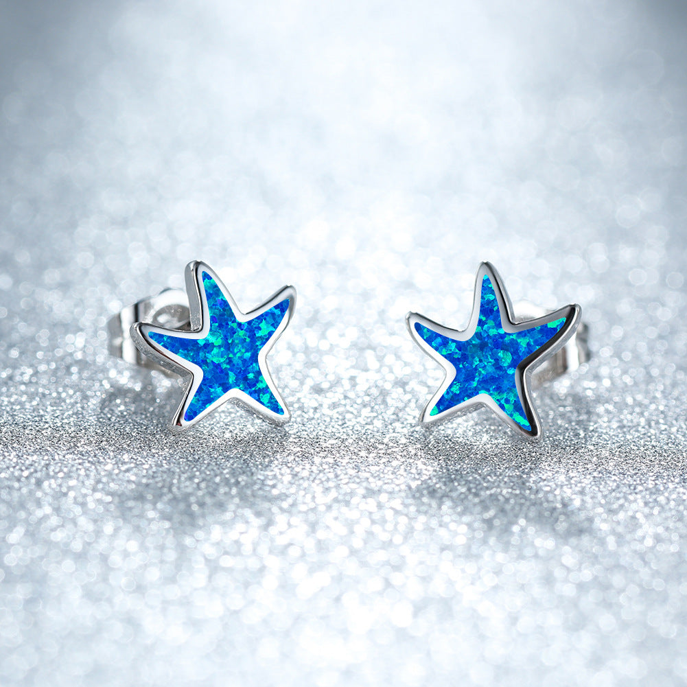 Close-up of blue opal starfish earrings with a silver finish against a sparkling background