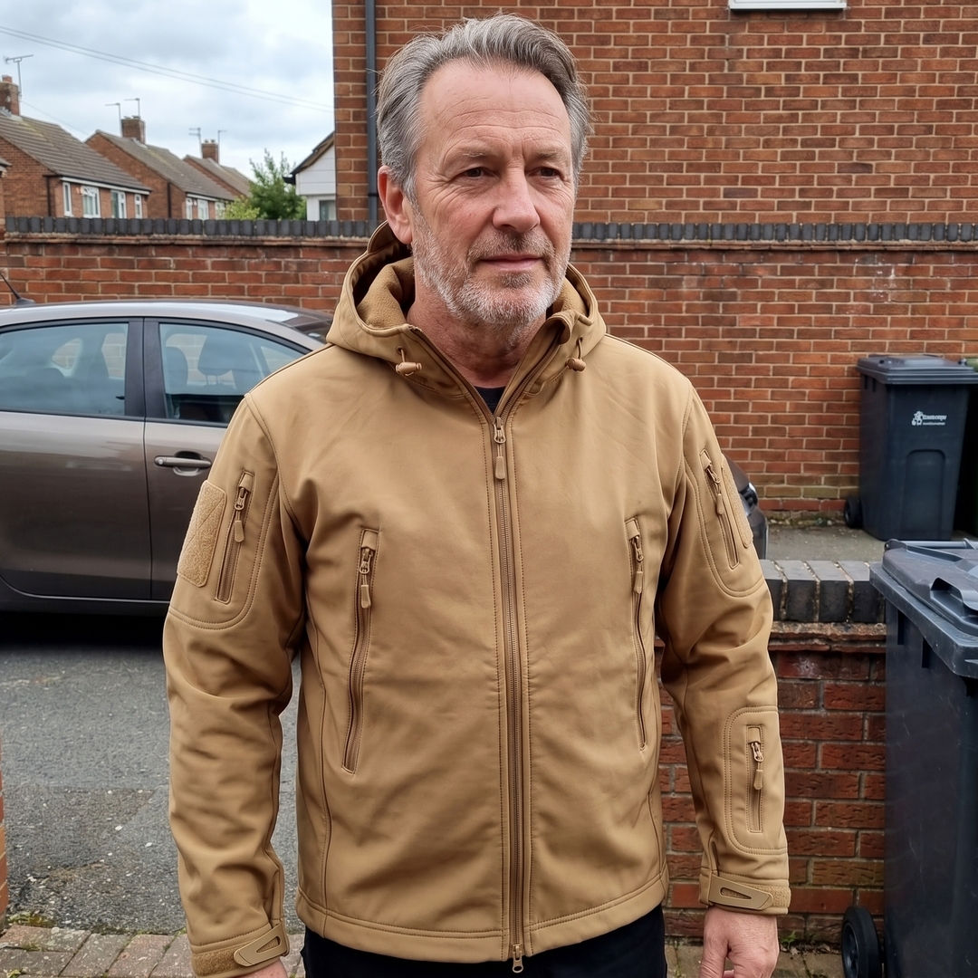 Man outdoors wearing khaki outdoor jacket near brick wall