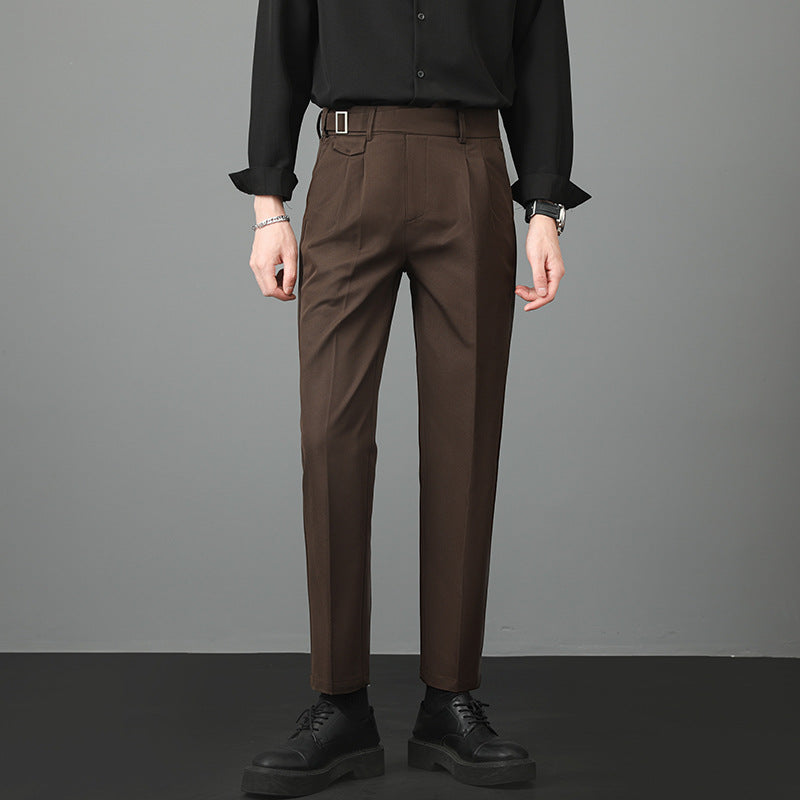Man standing in brown slim-fit straight-leg trousers paired with a dark shirt.