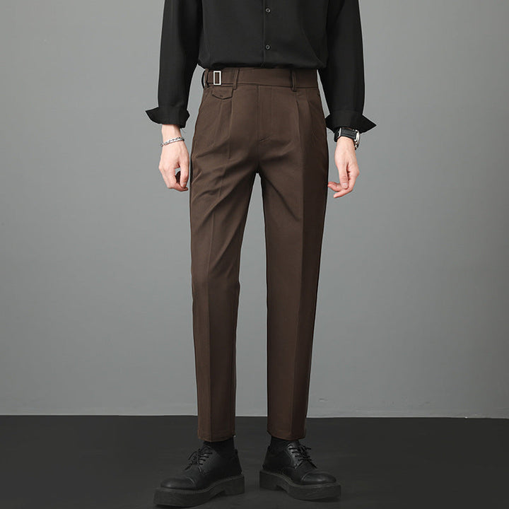 Man standing in brown slim-fit straight-leg trousers paired with a dark shirt.