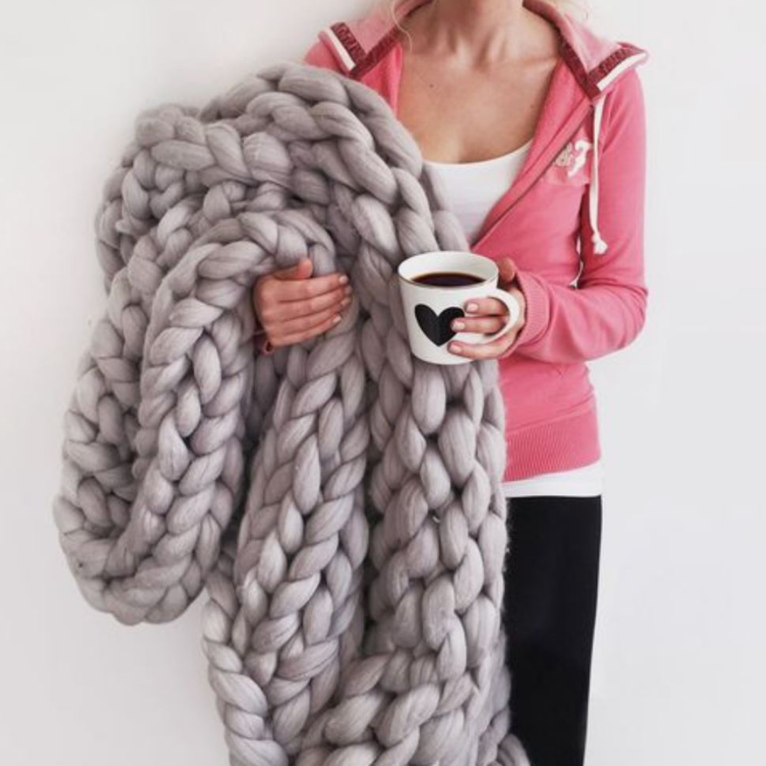 Person working on a DIY chunky knit blanket using soft yarn loops