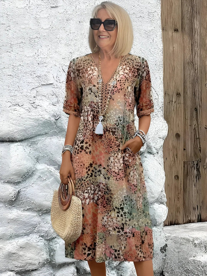 Mature woman wearing a sandy beige patterned mid-length dress with sunglasses and a straw bag