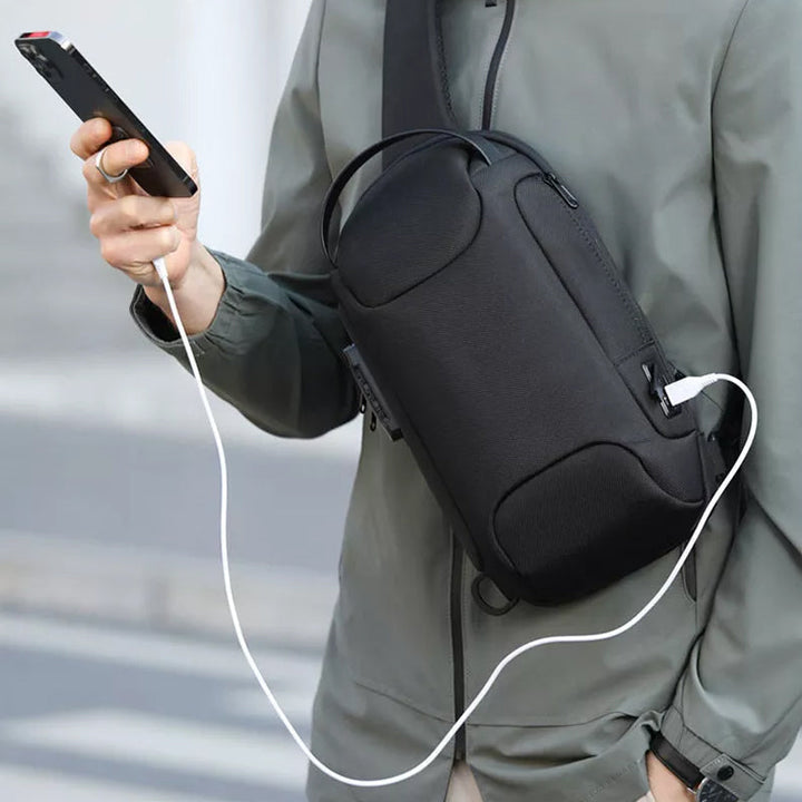 Person wearing black anti-theft waterproof crossbody bag while holding phone with connected cable