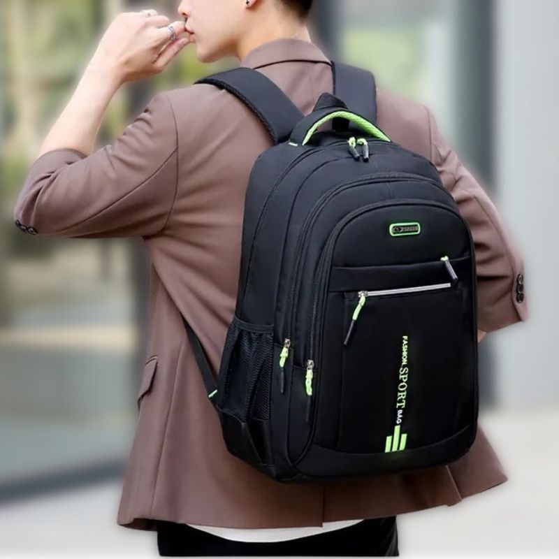 Man wearing a black urban backpack with green accent details on the shoulder straps and zipper pulls.