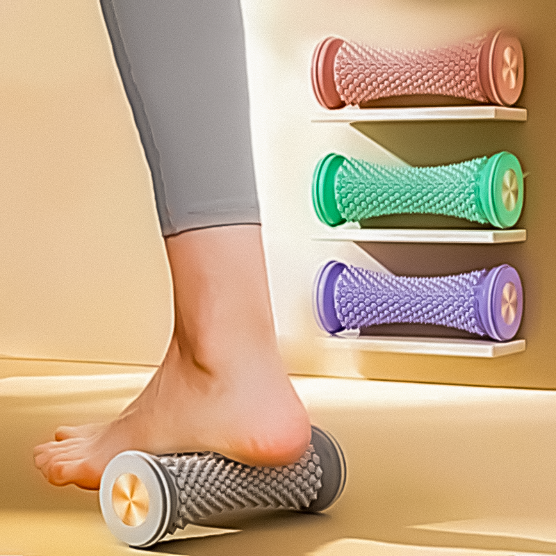 Foot resting on a grey massage roller with purple, cyan, and pink rollers displayed on a wall shelf