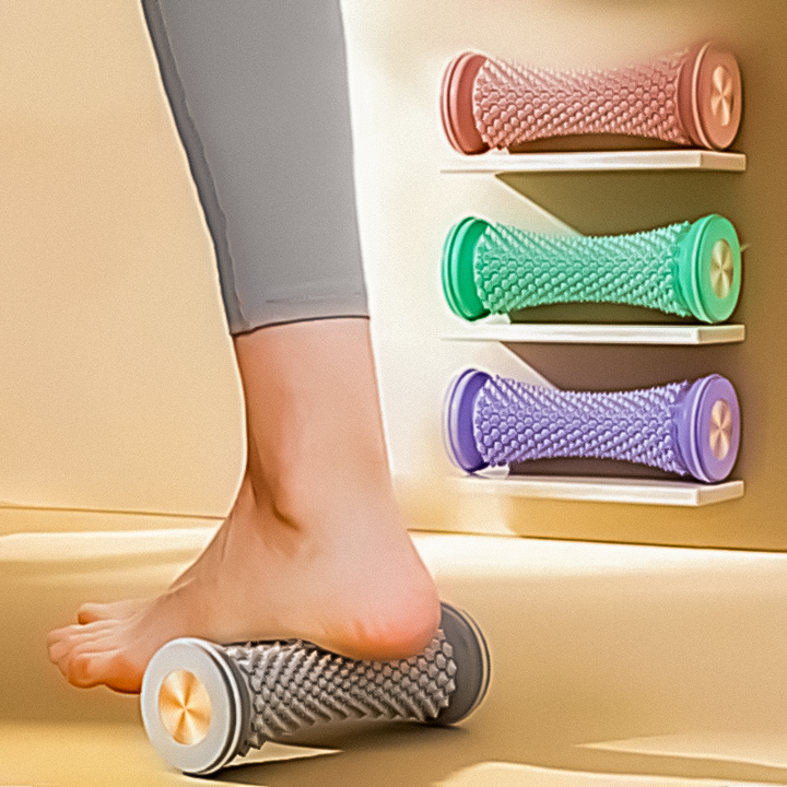 Foot resting on a grey massage roller with purple, cyan, and pink rollers displayed on a wall shelf