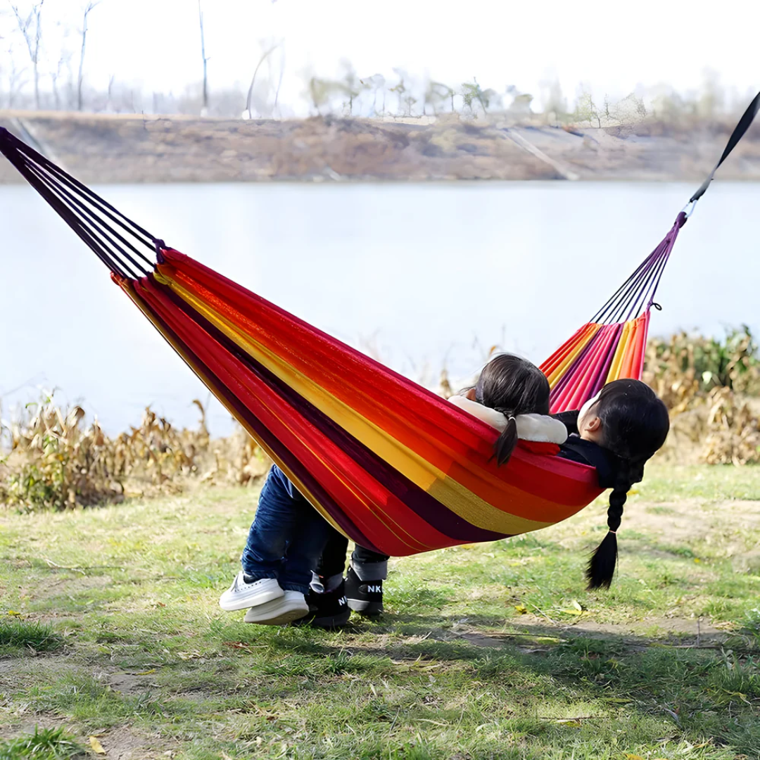 Two people relaxing together in a colorful outdoor hammock by the water