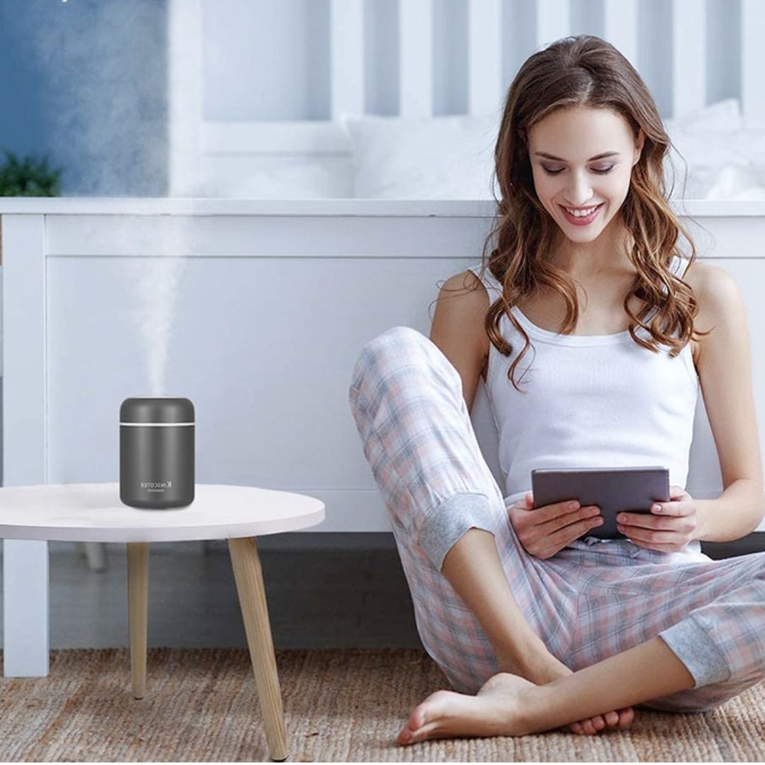 Woman relaxing in a bedroom next to a grey mini H2O humidifier