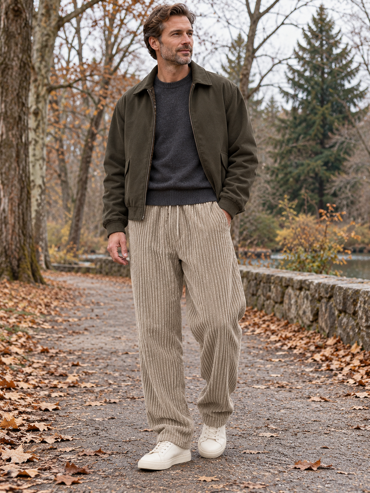 Full shot of a man walking outdoors in an autumn park wearing khaki trousers and a green jacket