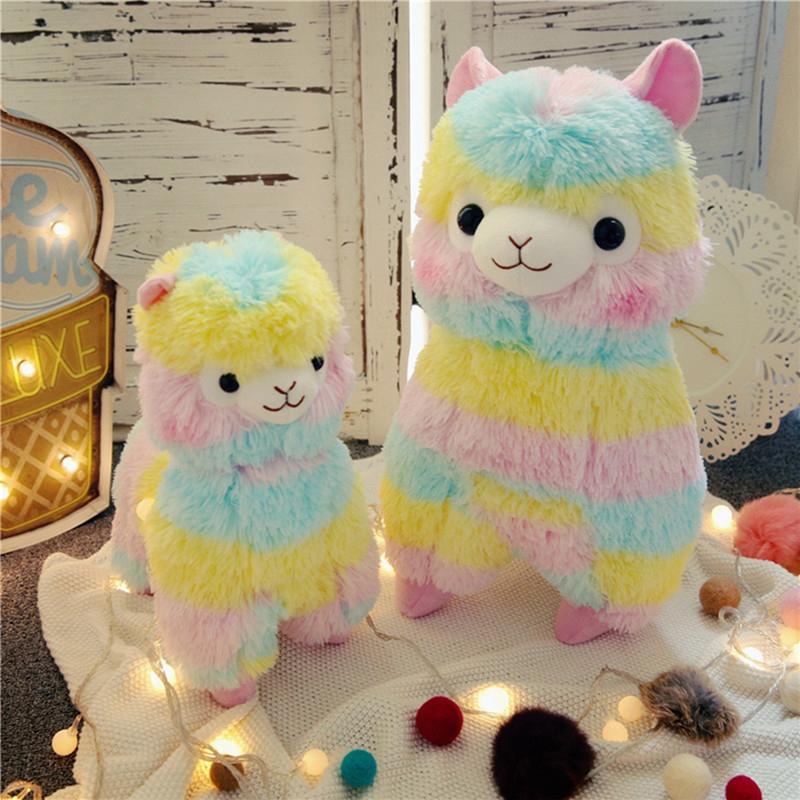 Two colorful rainbow alpaca plush toys sitting side by side on a cozy blanket