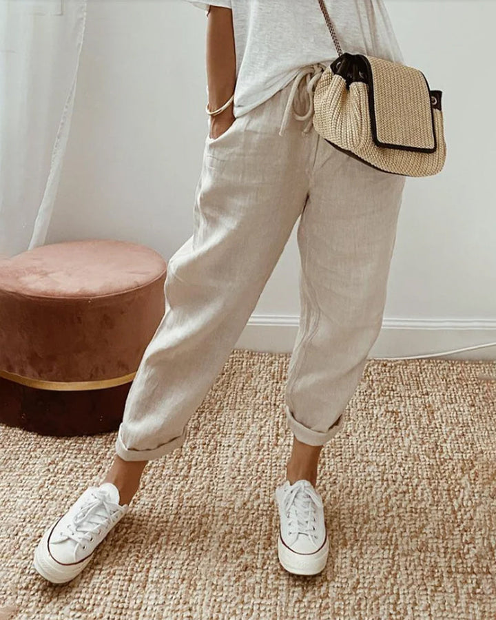 Woman wearing beige high-waist casual trousers with white sneakers and a woven crossbody bag