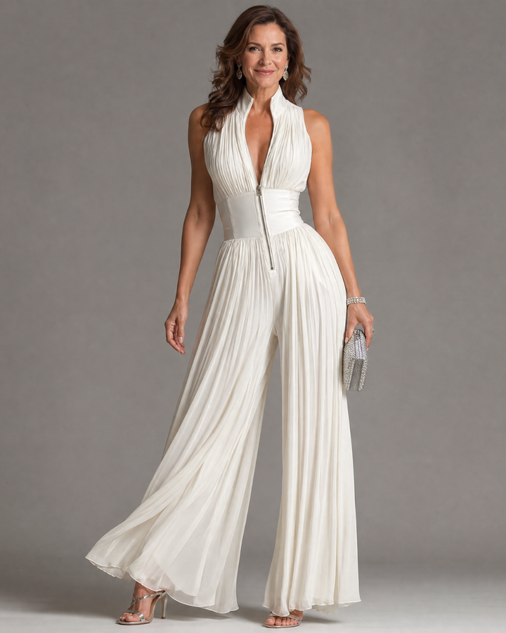 Woman posing gracefully in a white pleated halter neck wide-leg jumpsuit holding a silver clutch