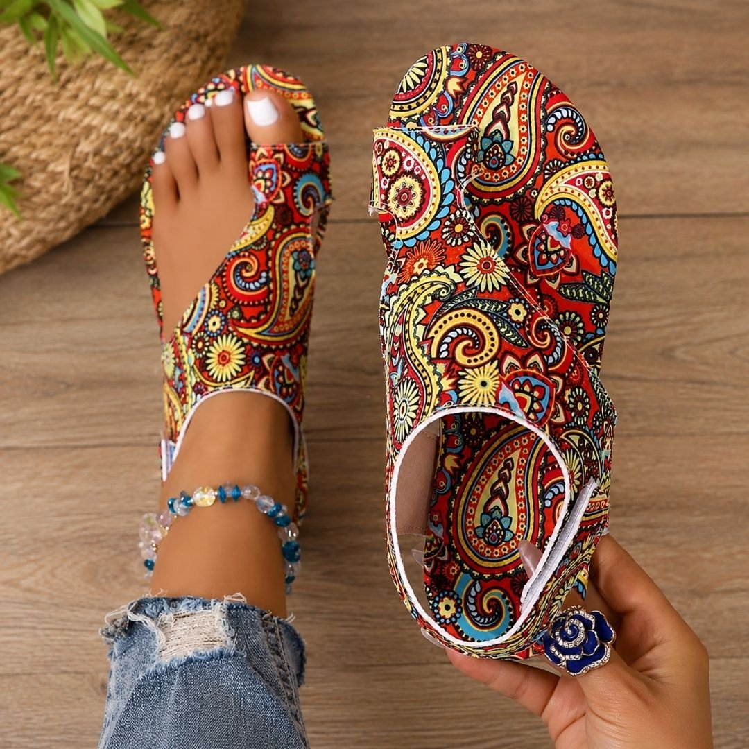 Woman holding red patterned orthopaedic sandal showcasing vibrant paisley design