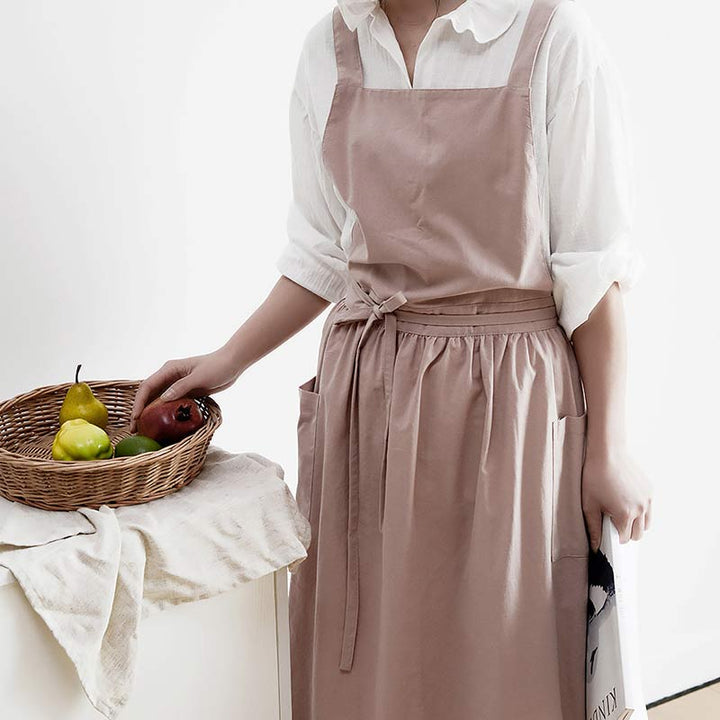 Woman wearing a stylish pink waterproof cross-back kitchen apron holding a fruit basket