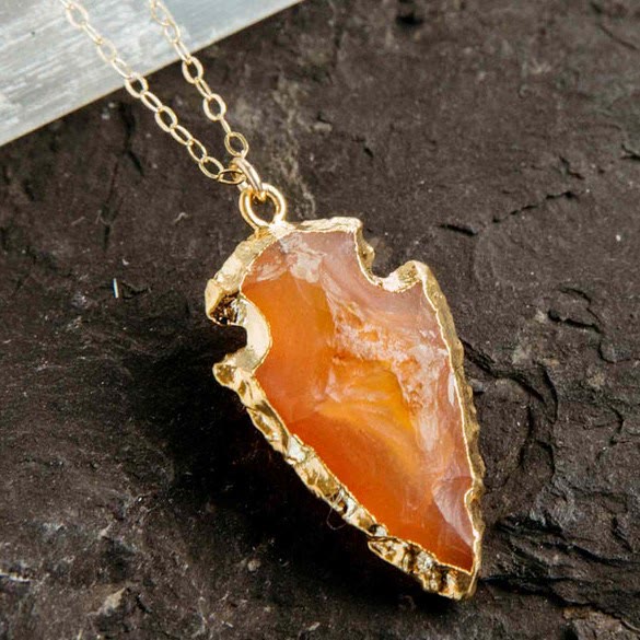Close-up of orange carnelian arrowhead crystal pendant on a gold chain
