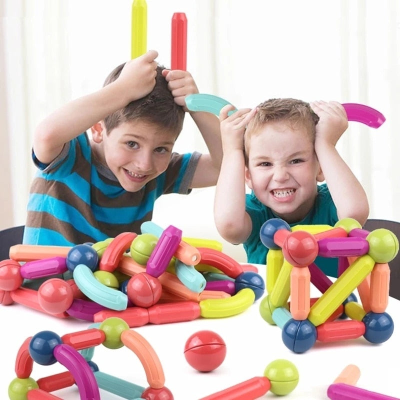 Two smiling boys playing with colorful magnetic building sticks and balls