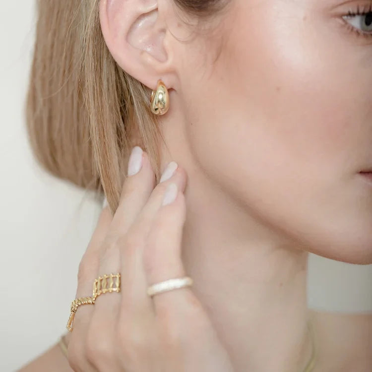 Close-up of a woman wearing polished gold drop earrings on her earlobe