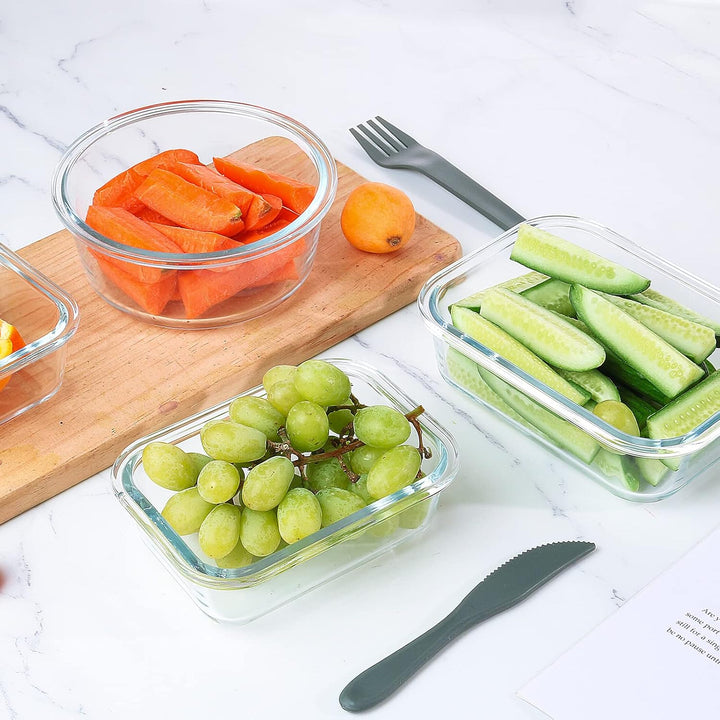 Glass food storage containers filled with fresh vegetables and fruit on a wooden board