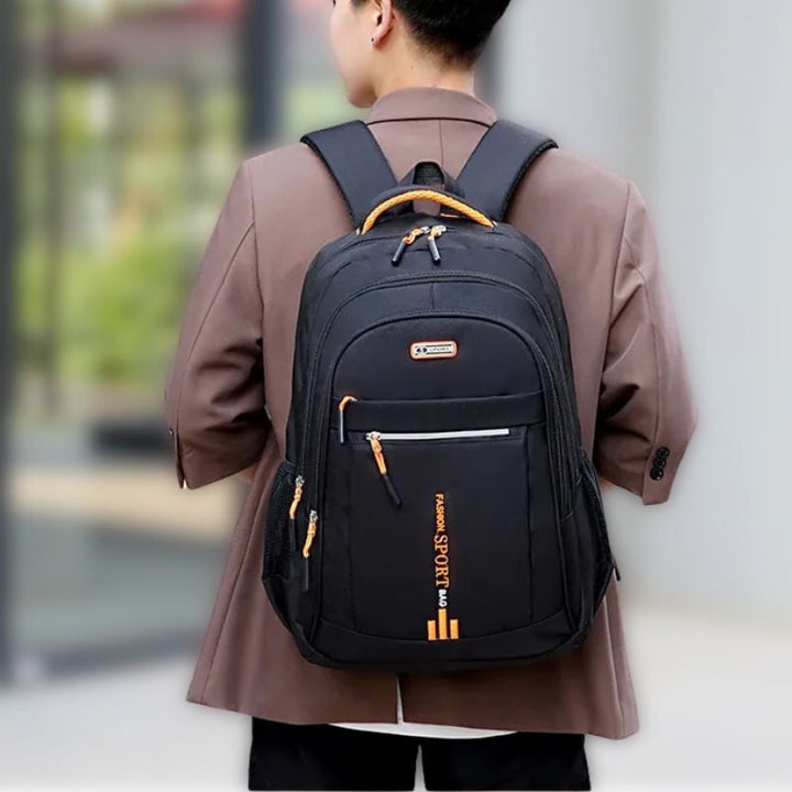 Man wearing a black commuter backpack featuring vibrant orange accent details on the handle and pulls.