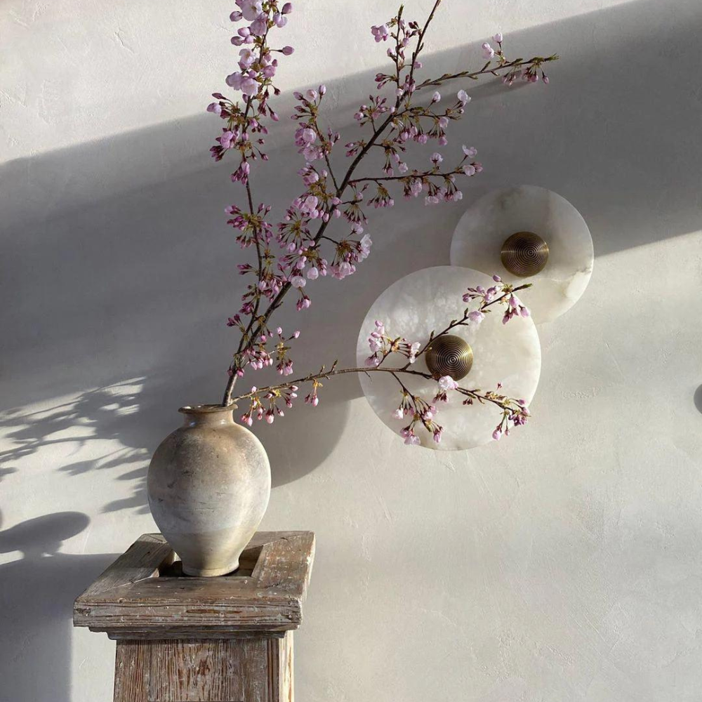 Two round alabaster wall lamps mounted on a neutral wall next to a floral vase.