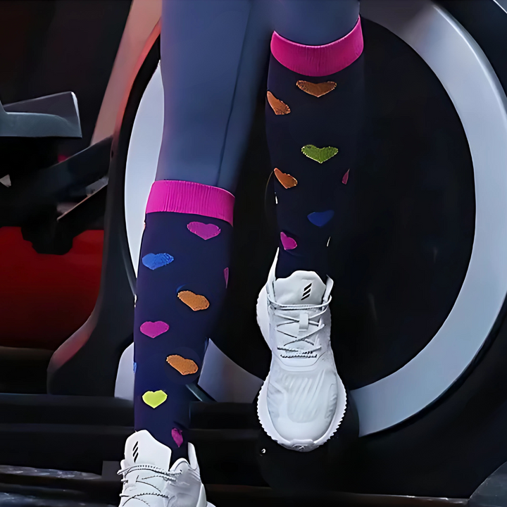 Close-up of a person wearing dark heart-patterned compression socks and white sneakers near a fitness machine
