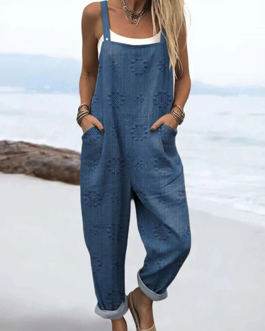 Model wearing blue meadow glow floral jumpsuit by the water