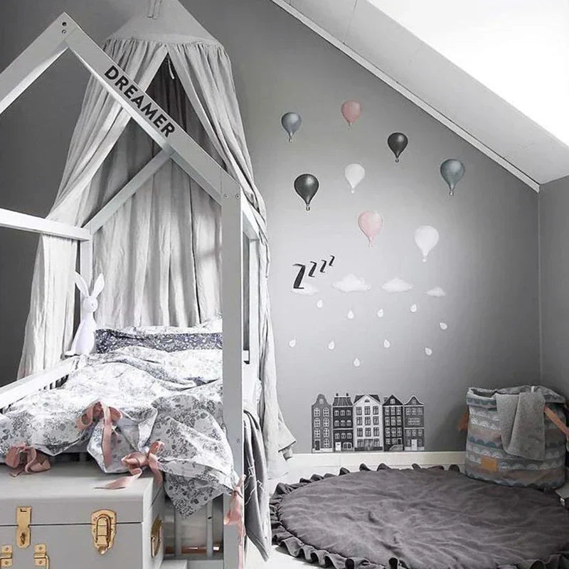 Dark gray round play mat neatly placed in a stylish children's bedroom featuring a wooden canopy bed and gray walls.