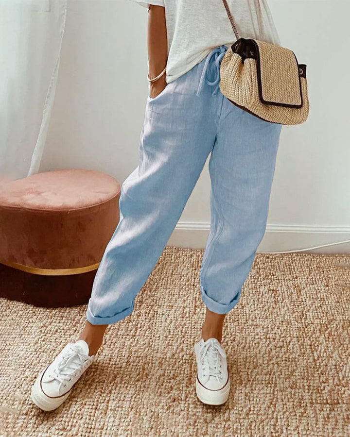 Woman wearing light blue high-waist casual trousers with white sneakers and a woven crossbody bag