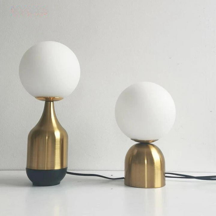 Nordic globe table lamp in brass and glass illuminating a modern bedside table.
