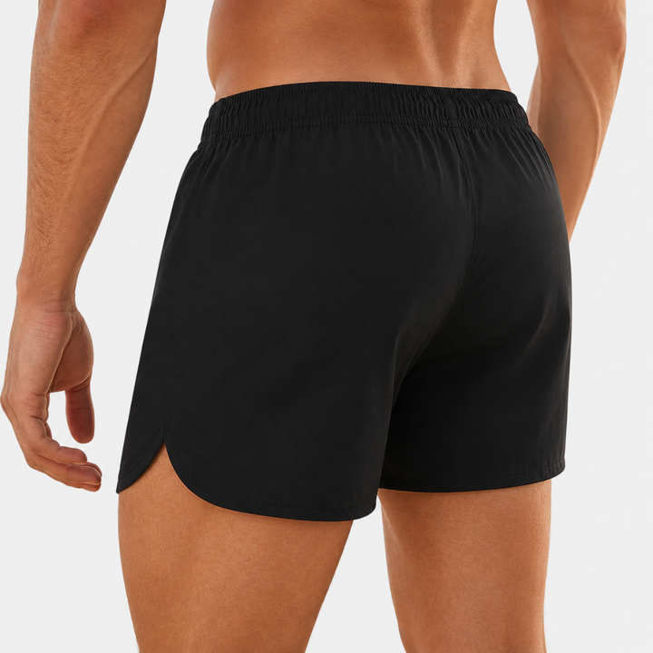 Back view of a man wearing black short swim shorts highlighting the tailored athletic fit.
