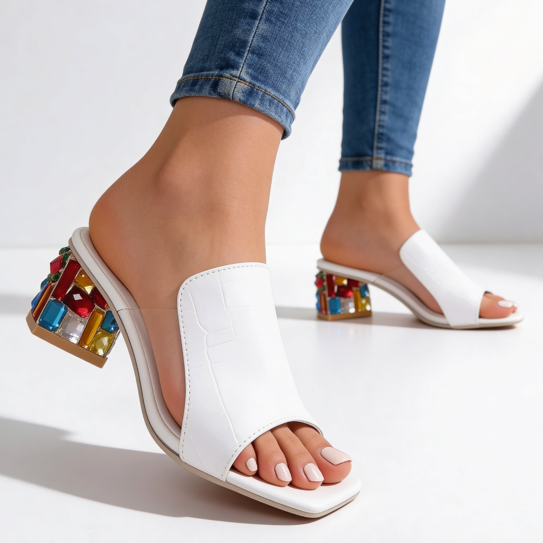 Side profile of white peep-toe slides featuring transparent side panels and jewel heel