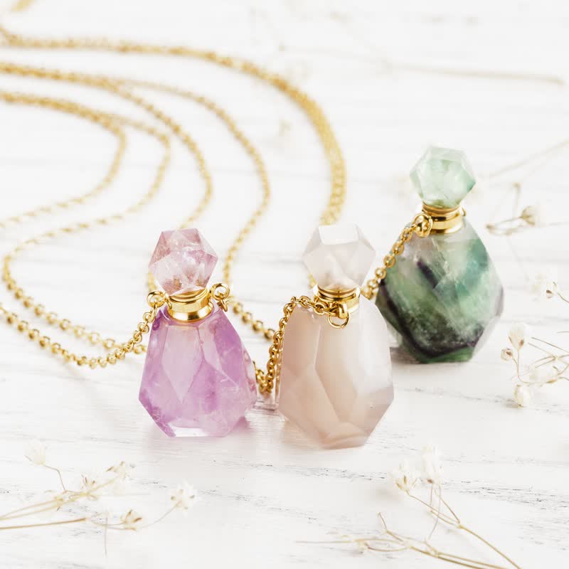Three faceted crystal perfume bottle necklaces with gold chains displayed on a white textured surface