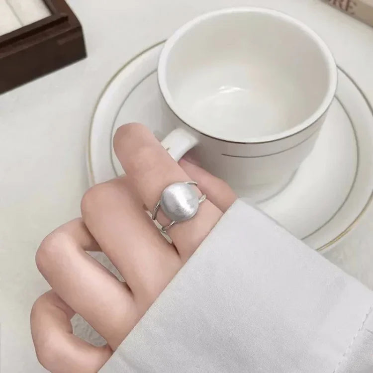 Close-up of a hand wearing the brushed silver half-dome ring next to a white teacup