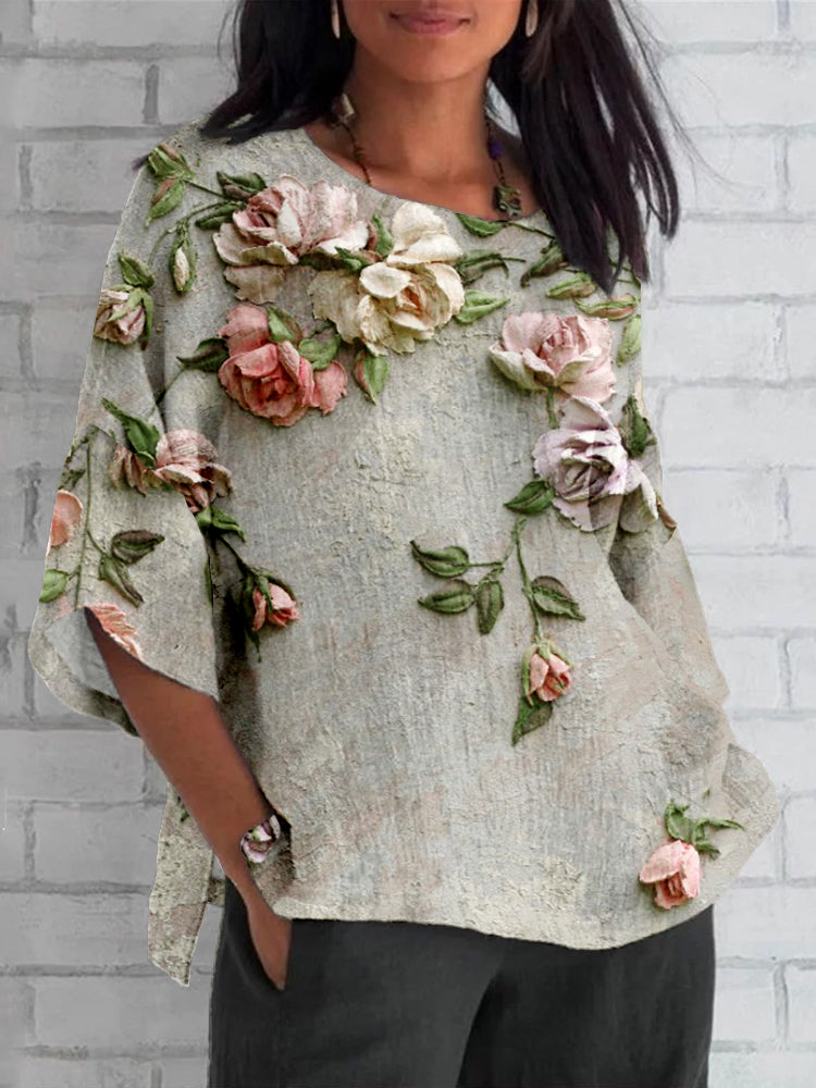 A woman wearing a light grey floral print top with dimensional flower details and three-quarter sleeves.
