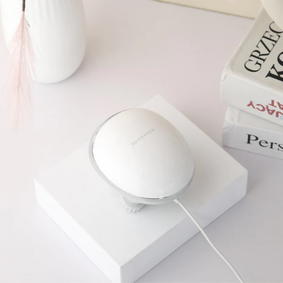 White electric scalp massager device resting on a white stand with books in the background